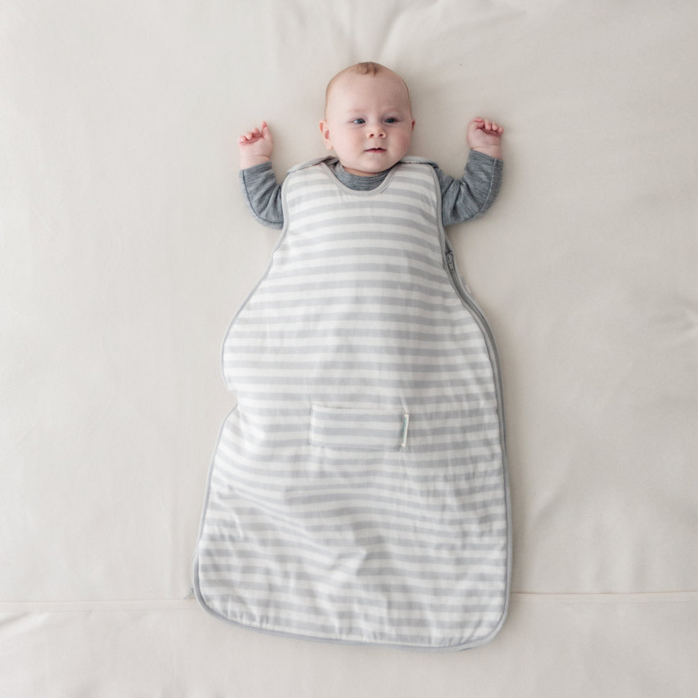Baby lying on a white surface wearing a gray and white striped sleep bag.