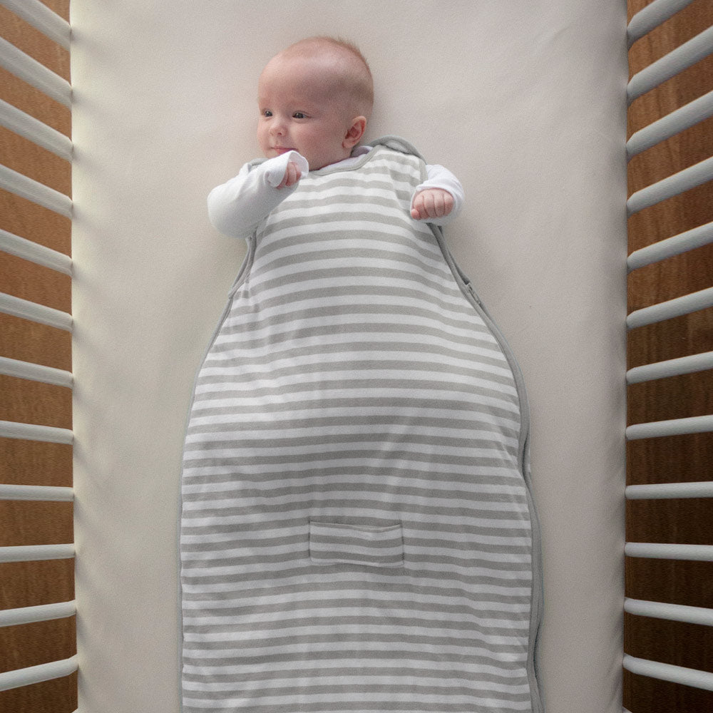 Baby wrapped in a gray and white striped swaddle in a crib.