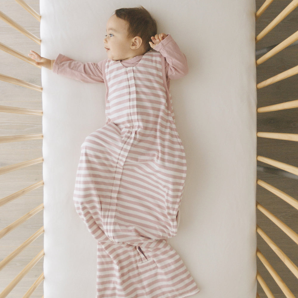 Baby in pink and white striped sleeping sack lying on a white surface with wooden slats in the background