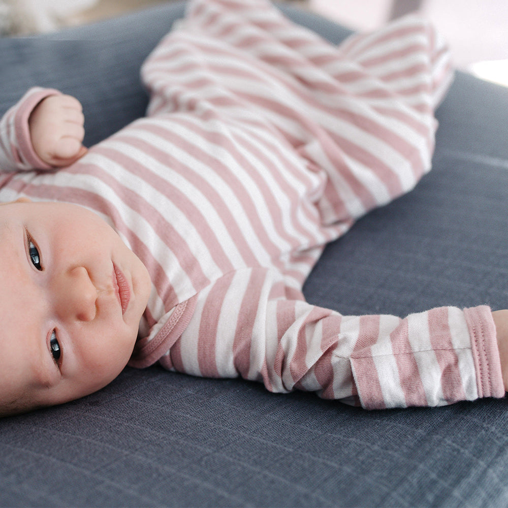 Baby wearing a pink and white striped  gown lying on a blue surface.
