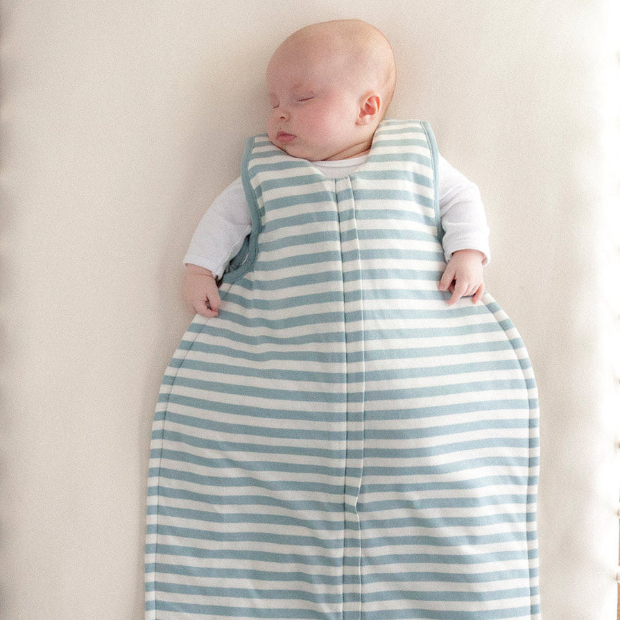 Baby sleeping in a blue and white striped onesie on a white surface.