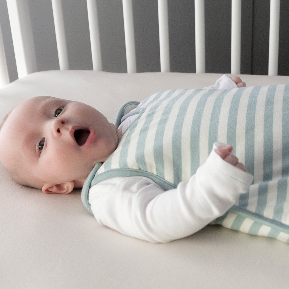 Baby lying in a crib with a striped swaddle blanket