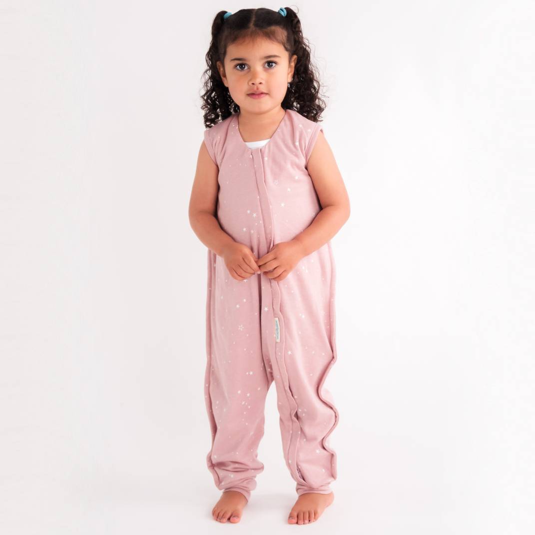 Young girl wearing a pink sleeveless woolbabe sleepsuit with white stars on a white background