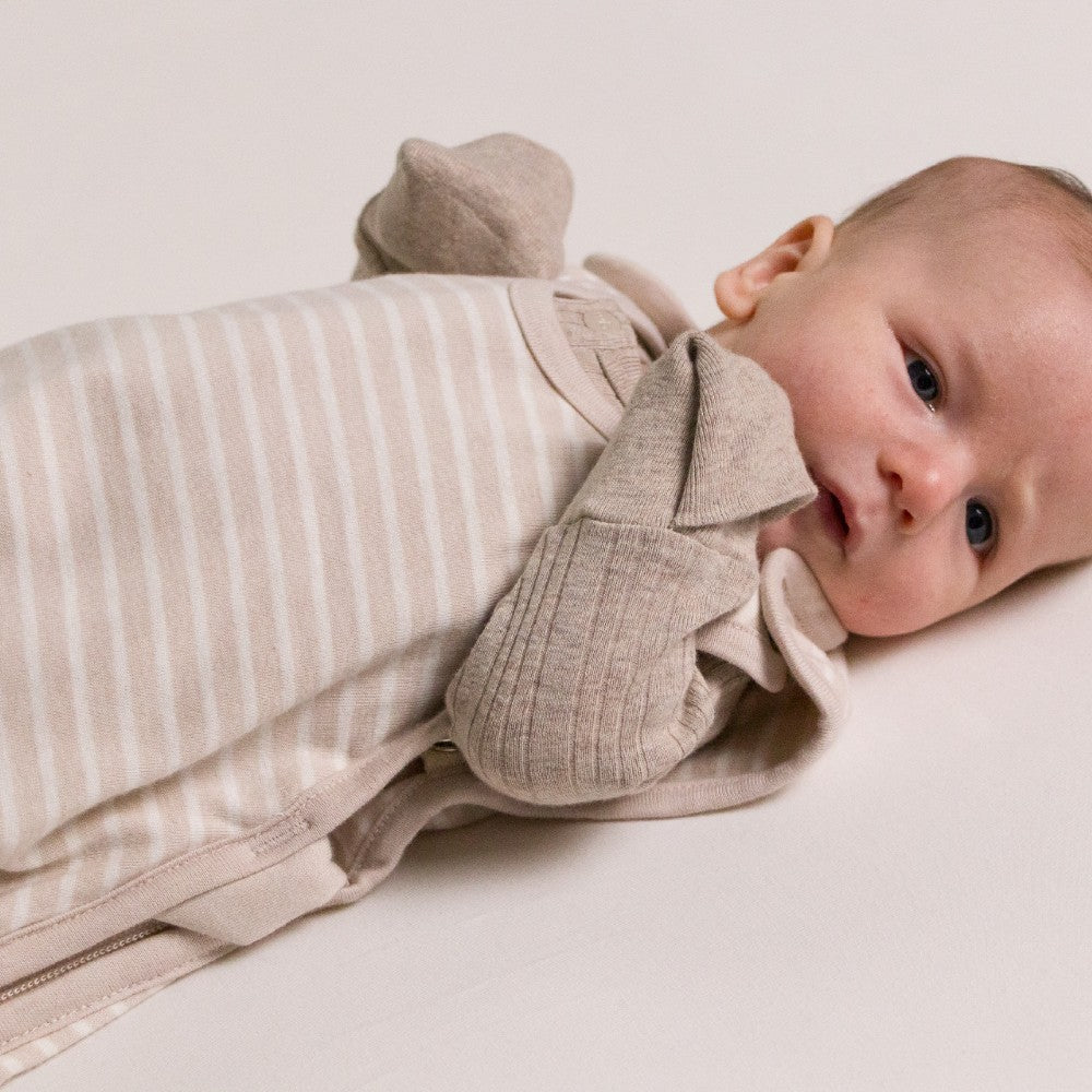 Baby wearing a beige outfit with striped pattern on a plain background