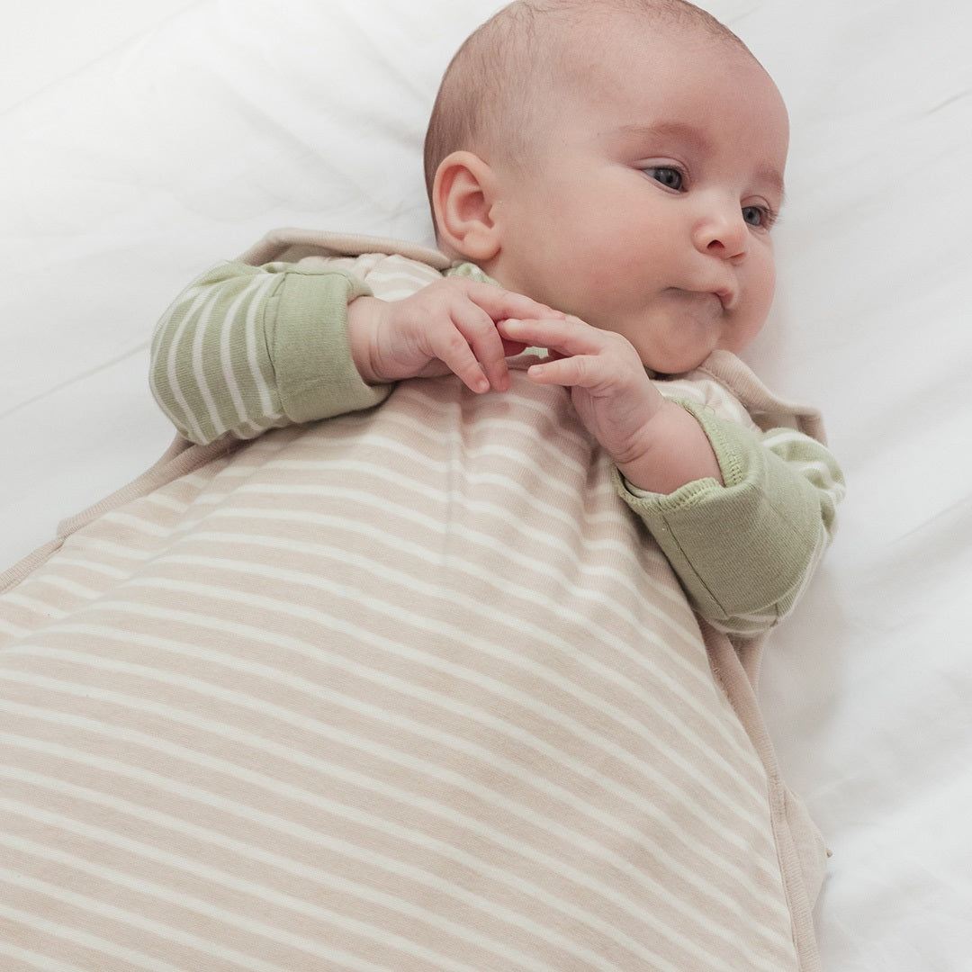 Baby wrapped in a beige and white striped swaddle with green sleeves on a white background