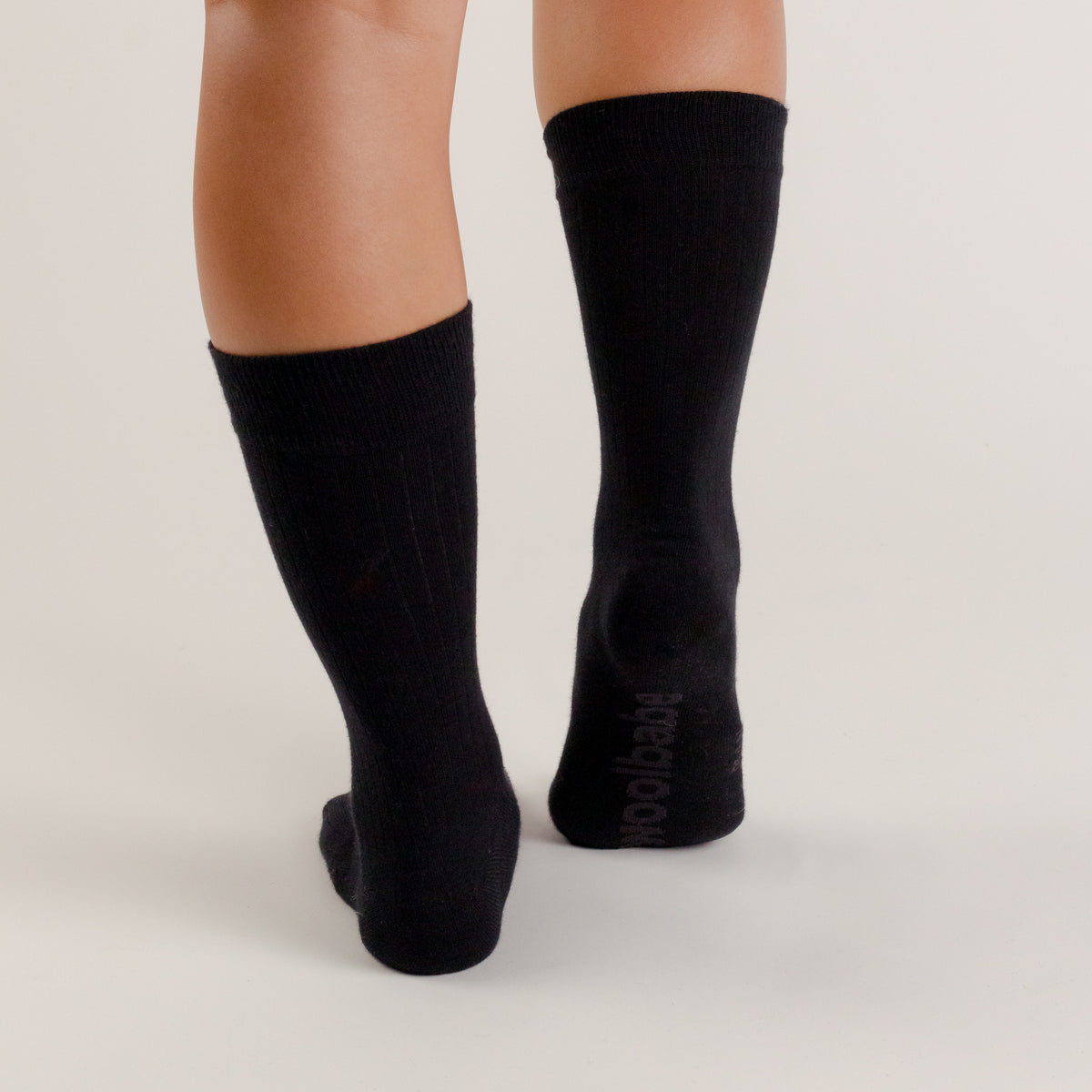 Black knee-high woolbabe socks worn by a person on a light gray background