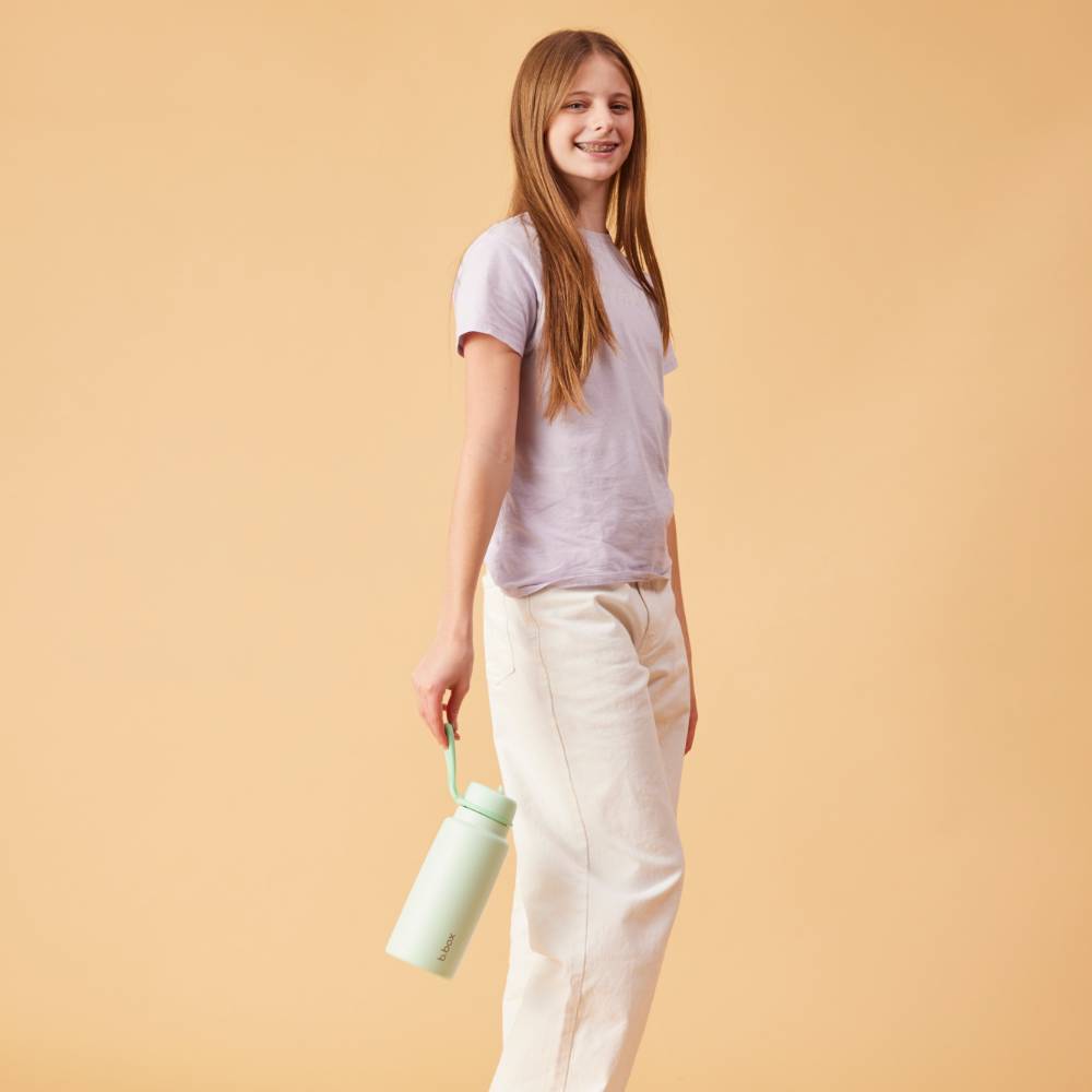 Young girl holding a light green water bottle against a beige background