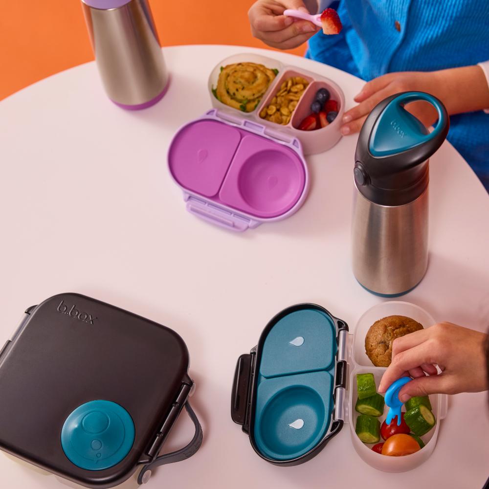 Children's lunchbox with snackbox set with compartments and food on a table.