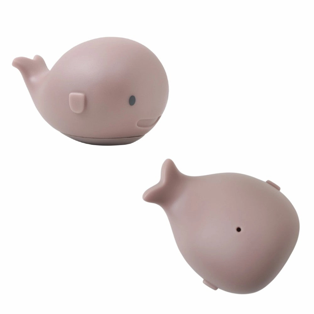 A minimalist whale-shaped bath toy shown from two angles on a plain white background. The item is a soft, matte dusty pink with tiny dark eyes and a small vent on the back.