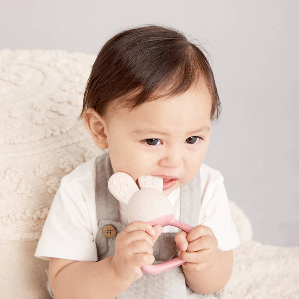 Baby holding a pink b.box teething toy with a neutral background