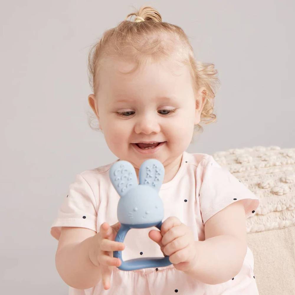 Child holding a blue bunny-shaped teething toy against a neutral background