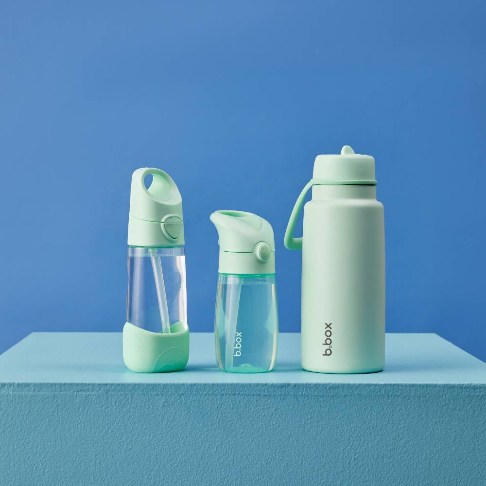 Three light mint green water bottles of different sizes and styles, including a straw bottle, a spout bottle, and a carry-handle insulated bottle, displayed on a light blue pedestal against a solid blue background.