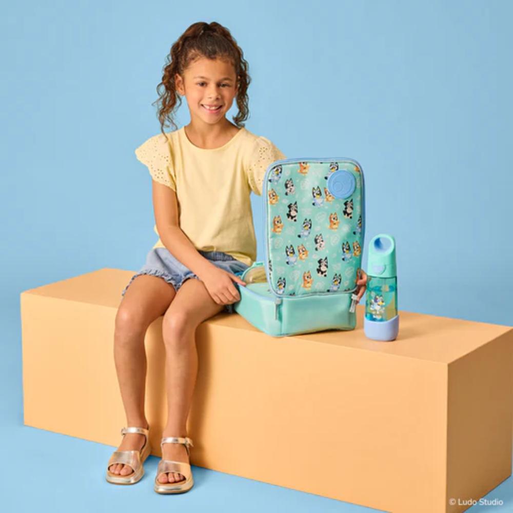 Girl sitting with an insulated lunch box and water bottle on a beige block against a blue background