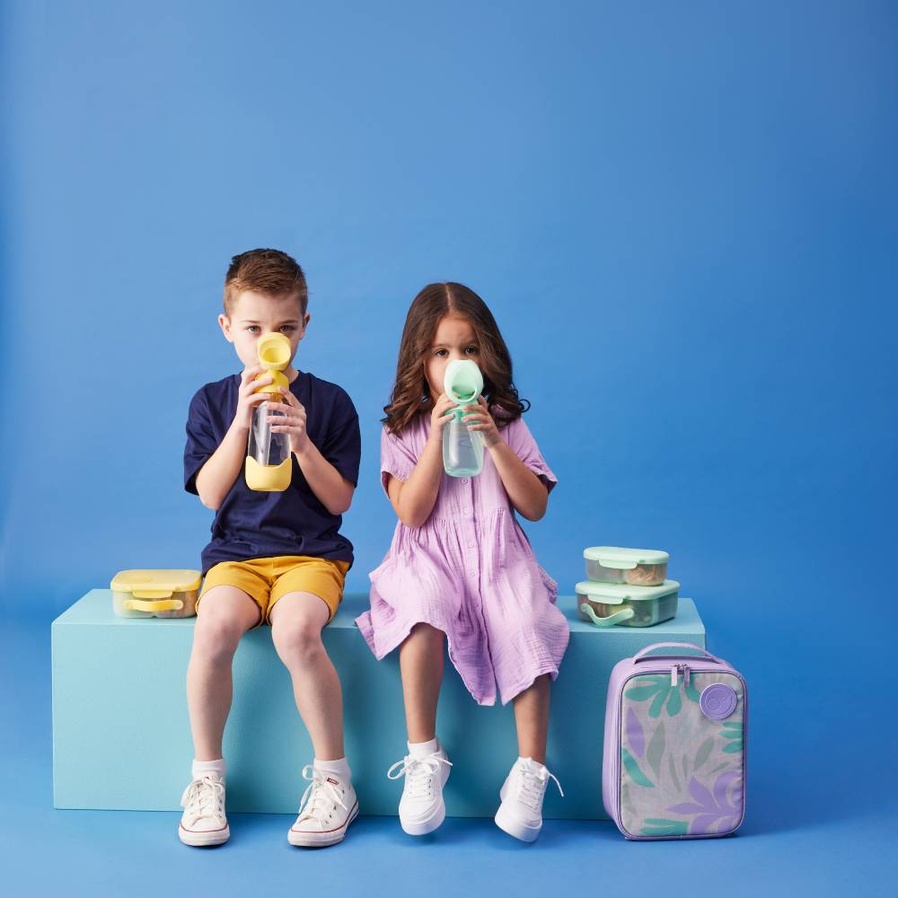 Two children sitting on a blue block with lunch bag against a blue background