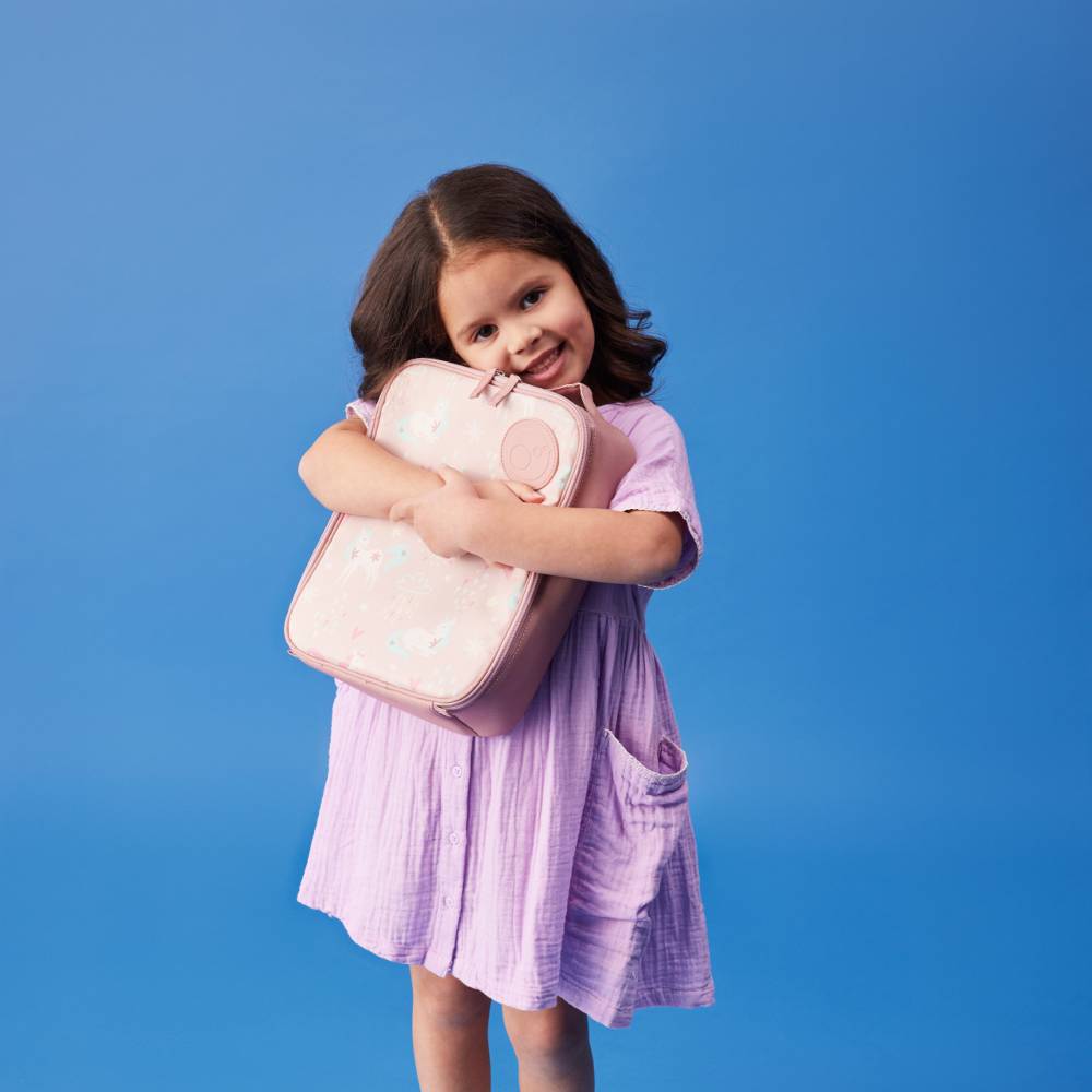 Young girl in a purple dress holding a pink insulated lunch bag against a blue background