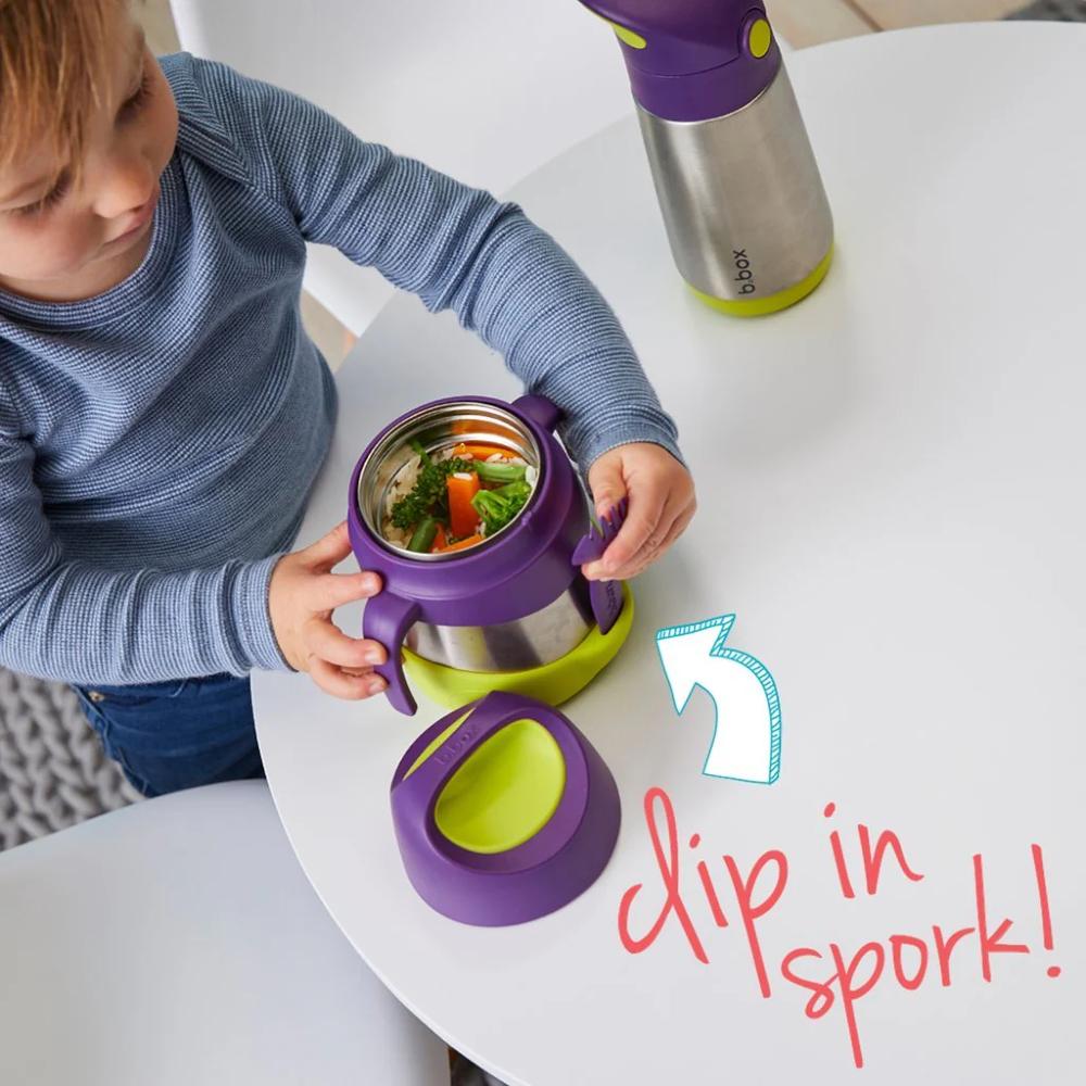 Child interacting with a b.box purple and green thermos-style container on a white table.