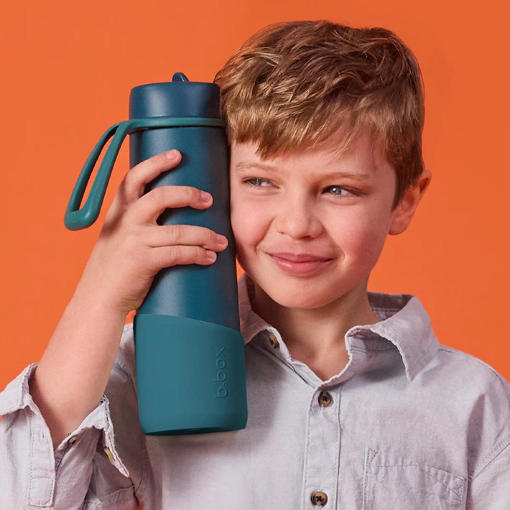 Child holding a teal green water bottle with a b.box logo against an orange background