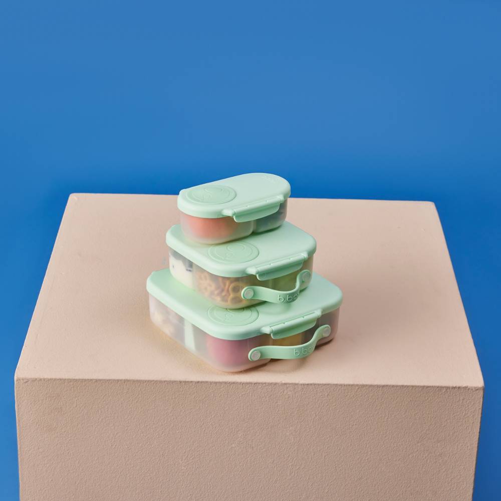 Stack of green b.box lunchboxes on a beige platform with a blue background