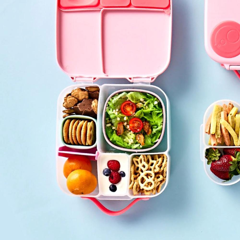Pink bento box with compartments filled with snacks and fruits on a light blue background