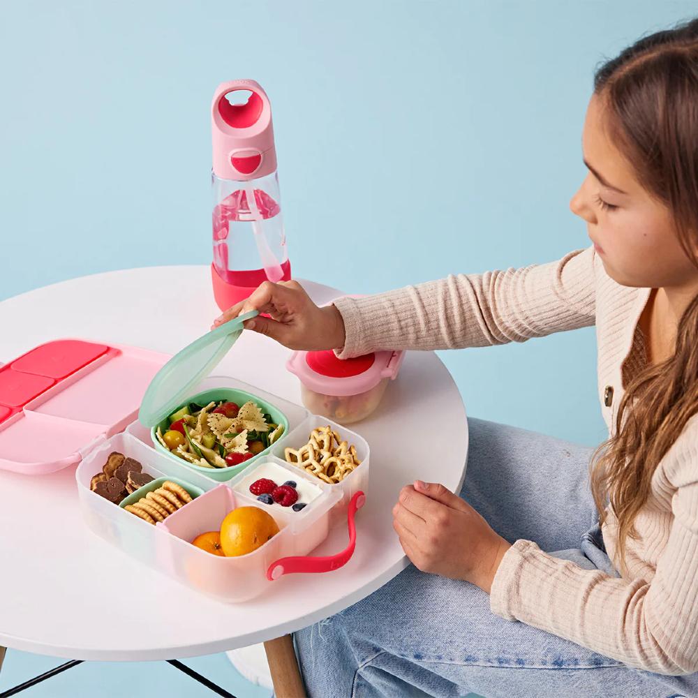 Girl sitting at a table with a lunchbox, bottle, and snacks on a light blue background