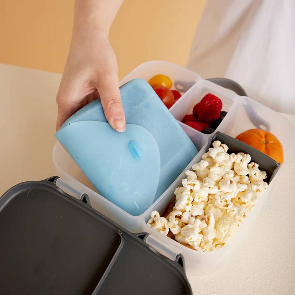 Hand packing a lunchbox with food pouch and with popcorn, berries, and other snacks.
