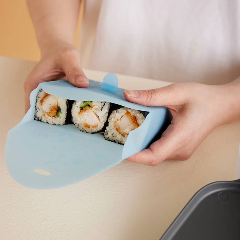 Hands using a blue silicone pouch to cover sushi rolls on a beige surface.