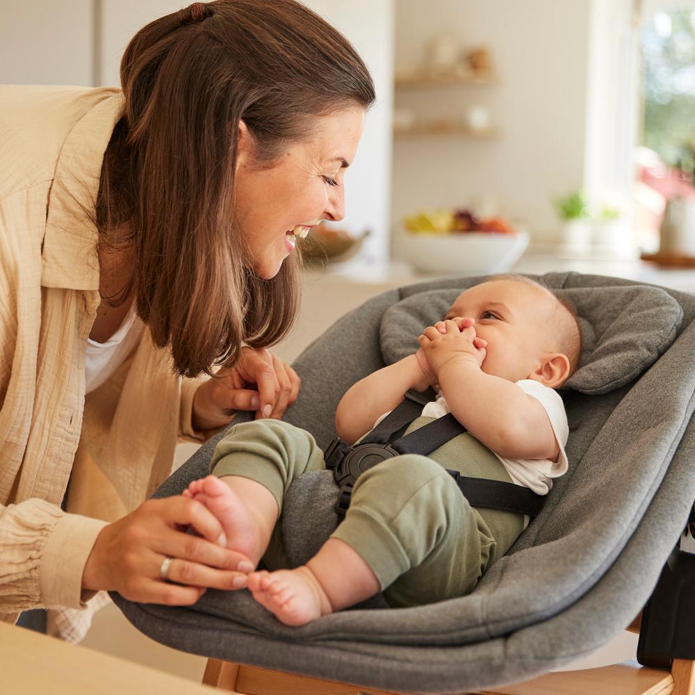 Woman holding a baby in a gray baby bouncer in a kitchen setting