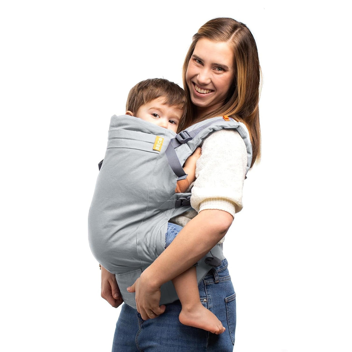 A woman wearing a light gray Beco Toddler carrier with a young child inside, photographed against a plain white background.
