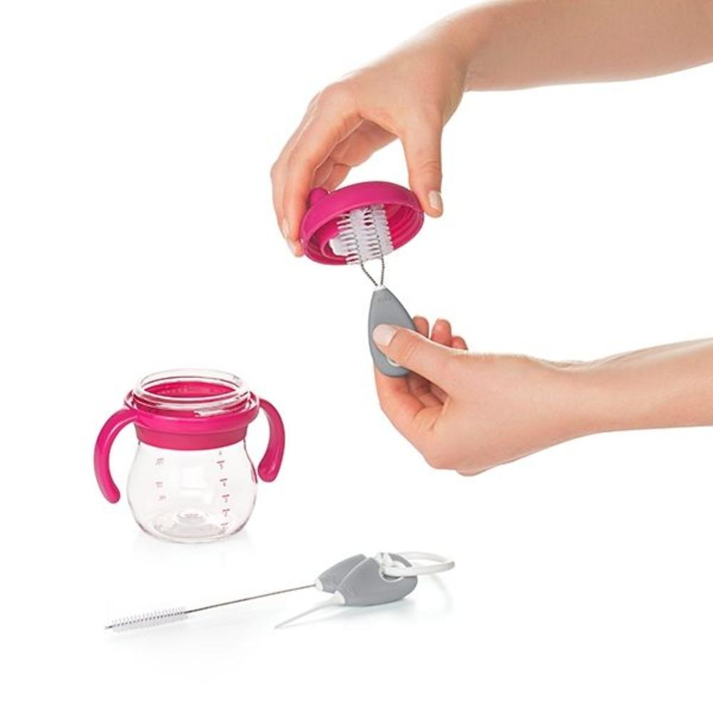 Two hands cleaning a sippy lid using a sippy cup cleaning brush. 
