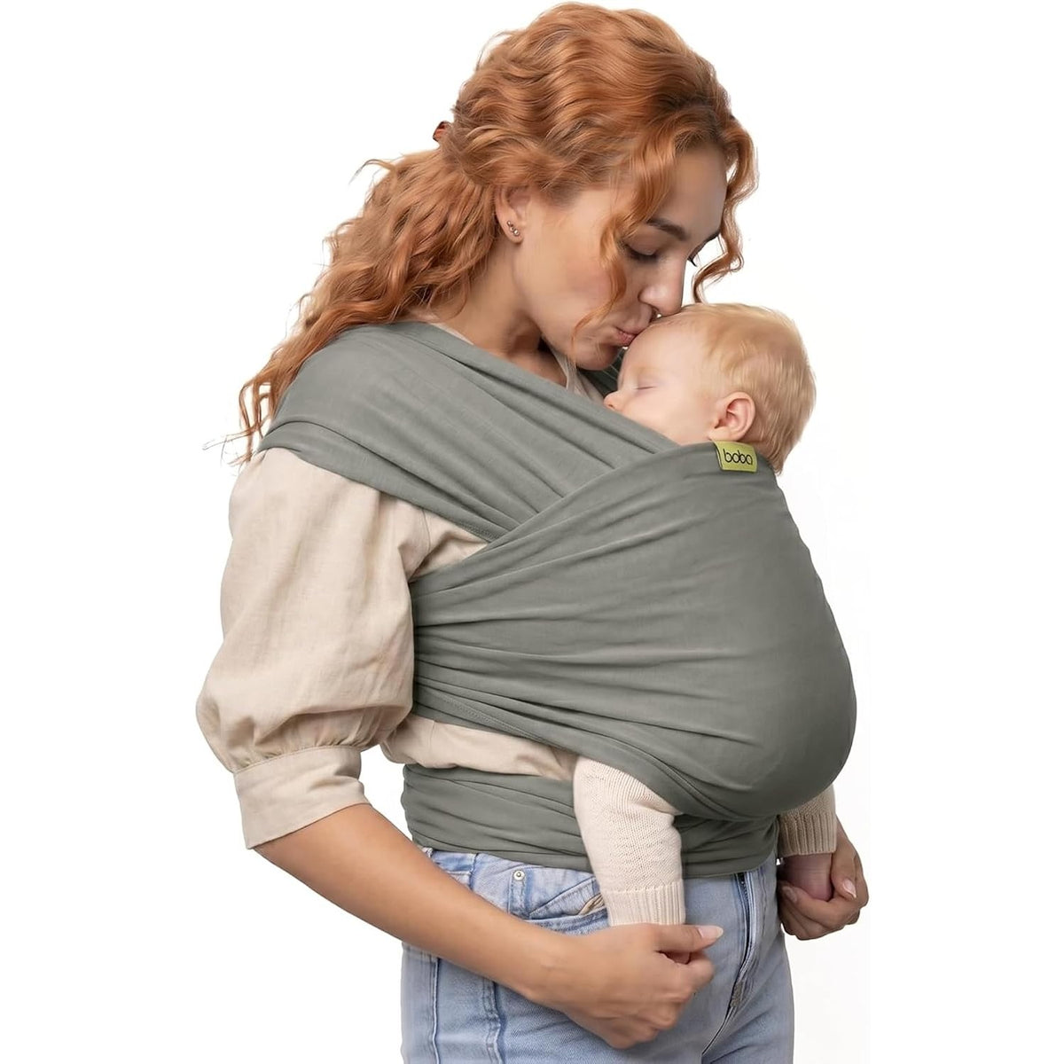 A woman with red hair wearing agreyish khaki wrap baby carrier with a baby, set against a plain white background.