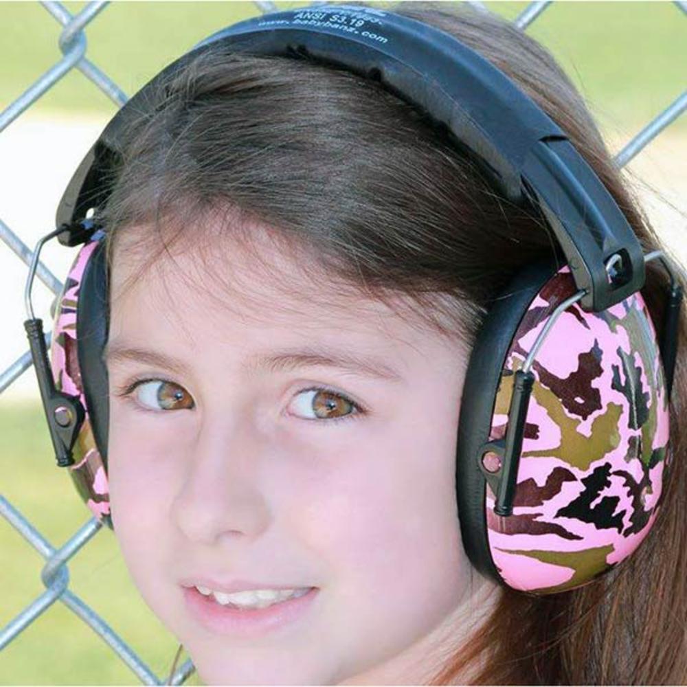 Child wearing pink and black camouflage ear protection against a chain-link fence background