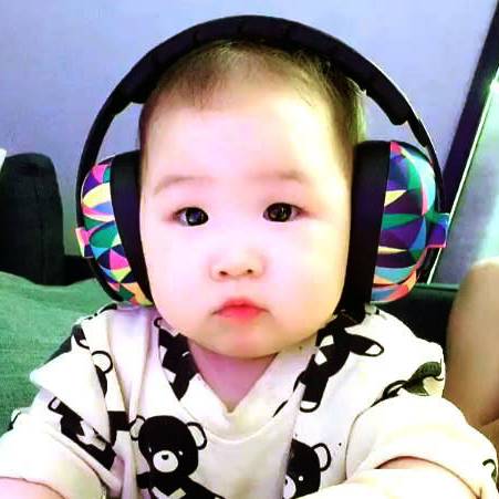 A baby wearing a white long-sleeve shirt with black cartoon bear prints and a colorful geometric-patterned earmuff
