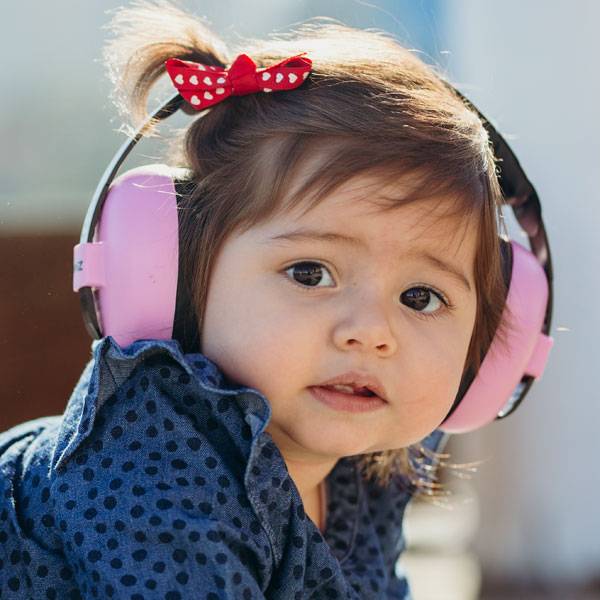 A close-up of a young child wearing pink over-ear headphones with a red bow with white polka dots in her hair, wearing a blue polka-dot top.