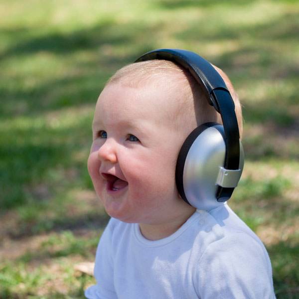 Baby wearing large headphones outdoors on a grassy background