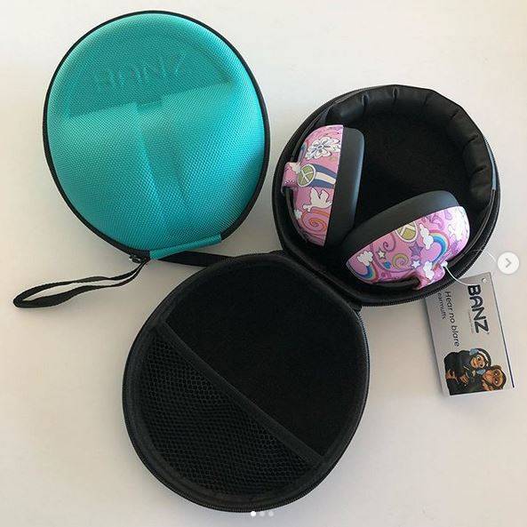 A pair of Banz over-ear headphones with pink and purple cartoon-patterned earcups, shown alongside a black zippered carrying case and a branded hangtag on a light background.