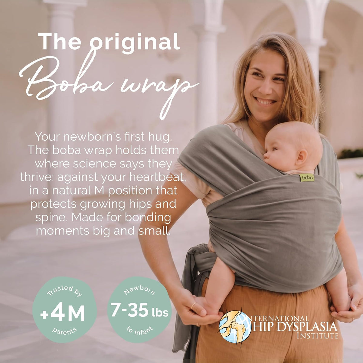 A woman wearing a gray Boba wrap baby carrier with a newborn baby inside, standing in a bright, sunlit architectural setting. The image includes promotional text about the wrap and logos for the International Hip Dysplasia Institute and Loopy.