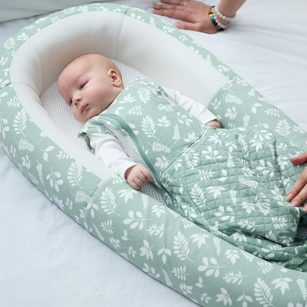 Purflo Fern baby bed with green print and white mesh base with baby in swaddle