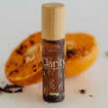 A small cylindrical roll-on bottle labeled &Honey 'Clarity' with a bamboo cap, standing in front of blurred orange slices on a light background.