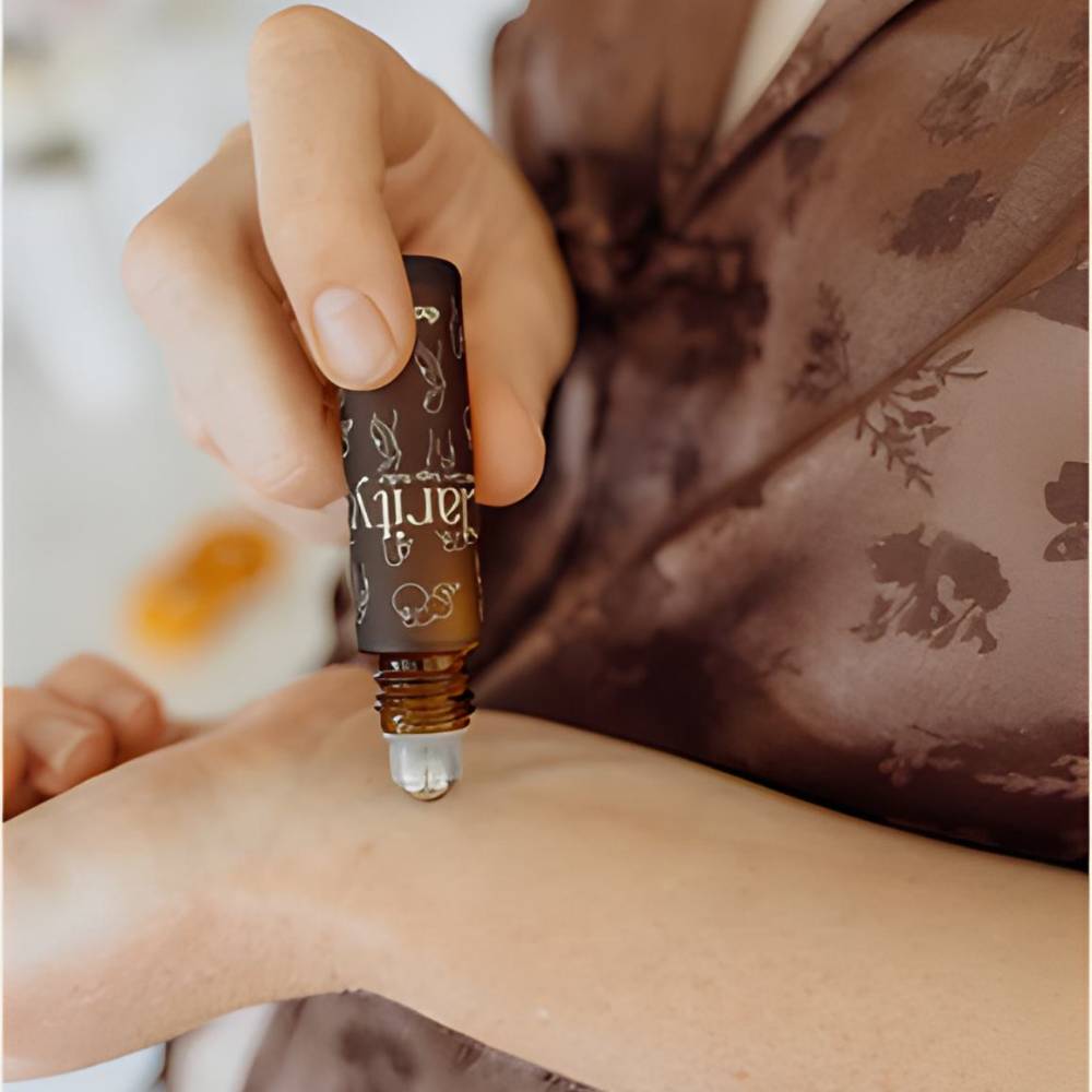 A close-up of a hand holding a small roll-on bottle of Clarity on her wrist with a brown floral robe in the background.