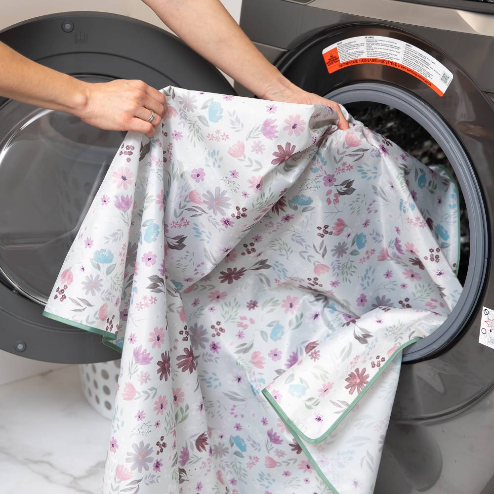 A light grey and floral splat mat with sage green piping being placed into a grey washing machine 