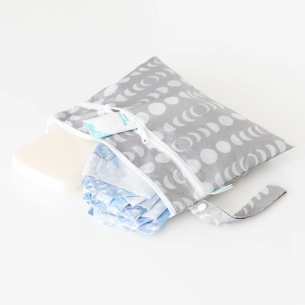 Nappies and wipes inside a grey wet and dry clutch with white moon phase pattern on a white background