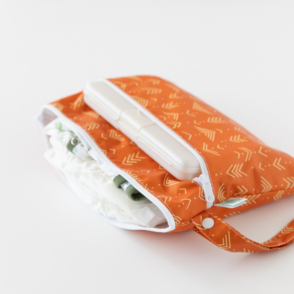 Nappies, clothing and wipes inside an orange wet and dry clutch with yellow line pattern on a white background 