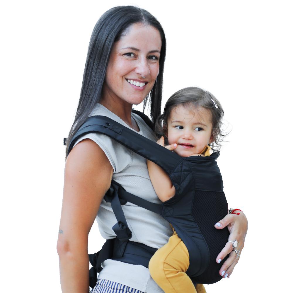 Woman carrying a child in a black mesh travel baby carrier against a white background