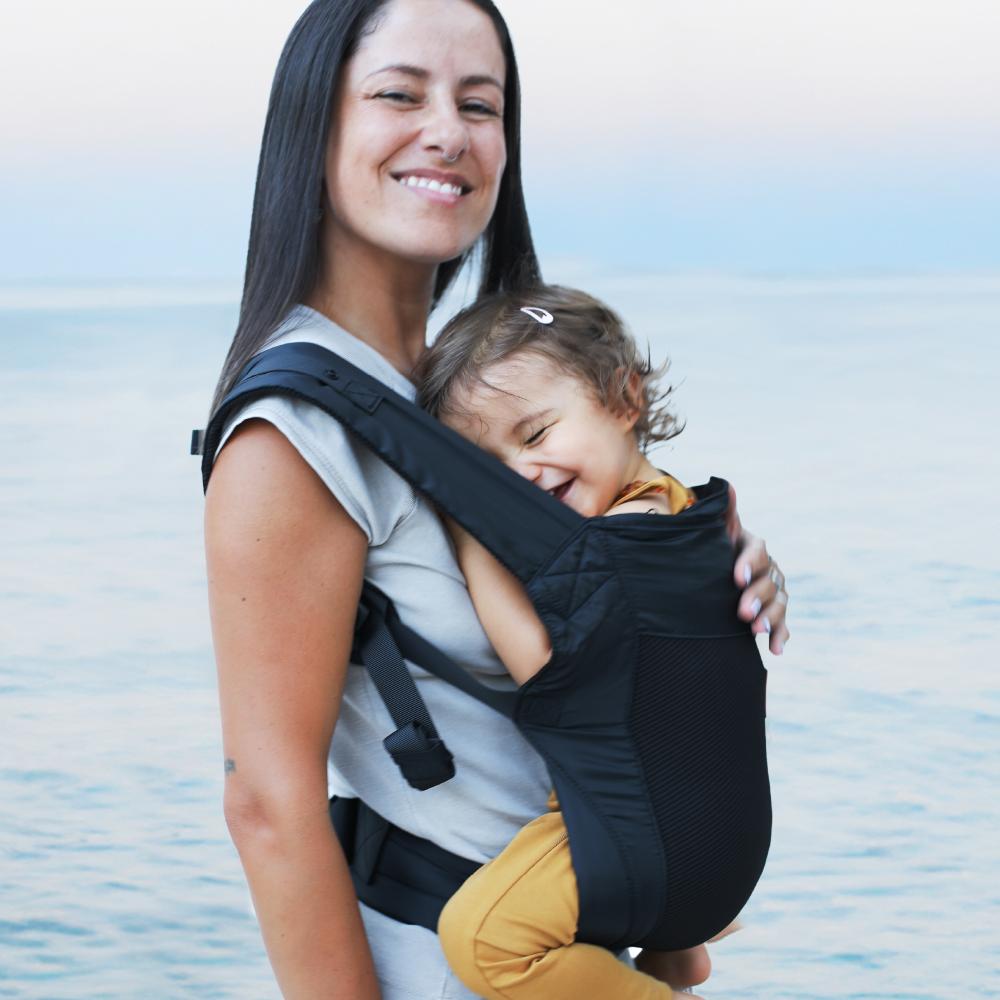Woman carrying baby on her front in a mesh Beco Fly travel carrier
