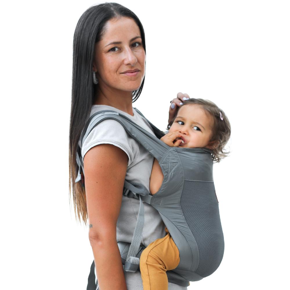 Woman carrying a baby in a gray mesh travel baby carrier against a white background
