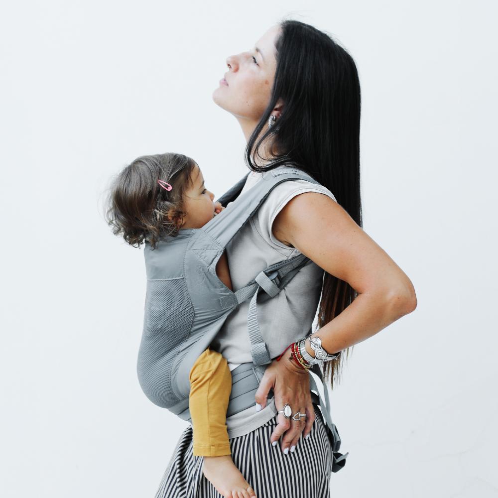 Woman carrying a child in a mesh summer baby carrier against a white background