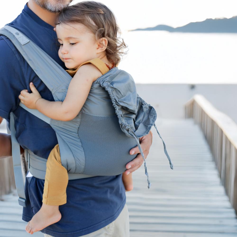 Man holding a child in a lighweight mesh baby carrier by a waterfront