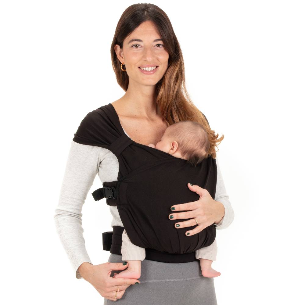 Woman holding a baby in a black baby carrier against a white background