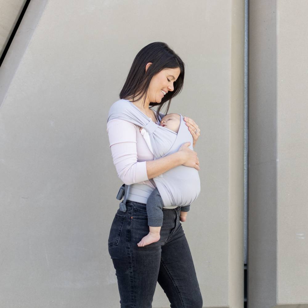 Woman carrying a baby in a sling against a plain background