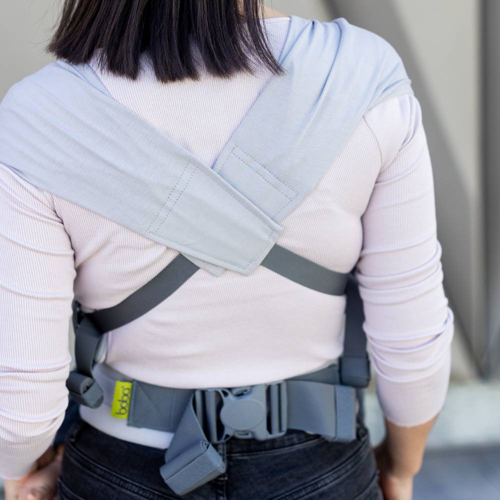 Person wearing a gray Boba Bliss baby carrier showing the straps crossed on the back